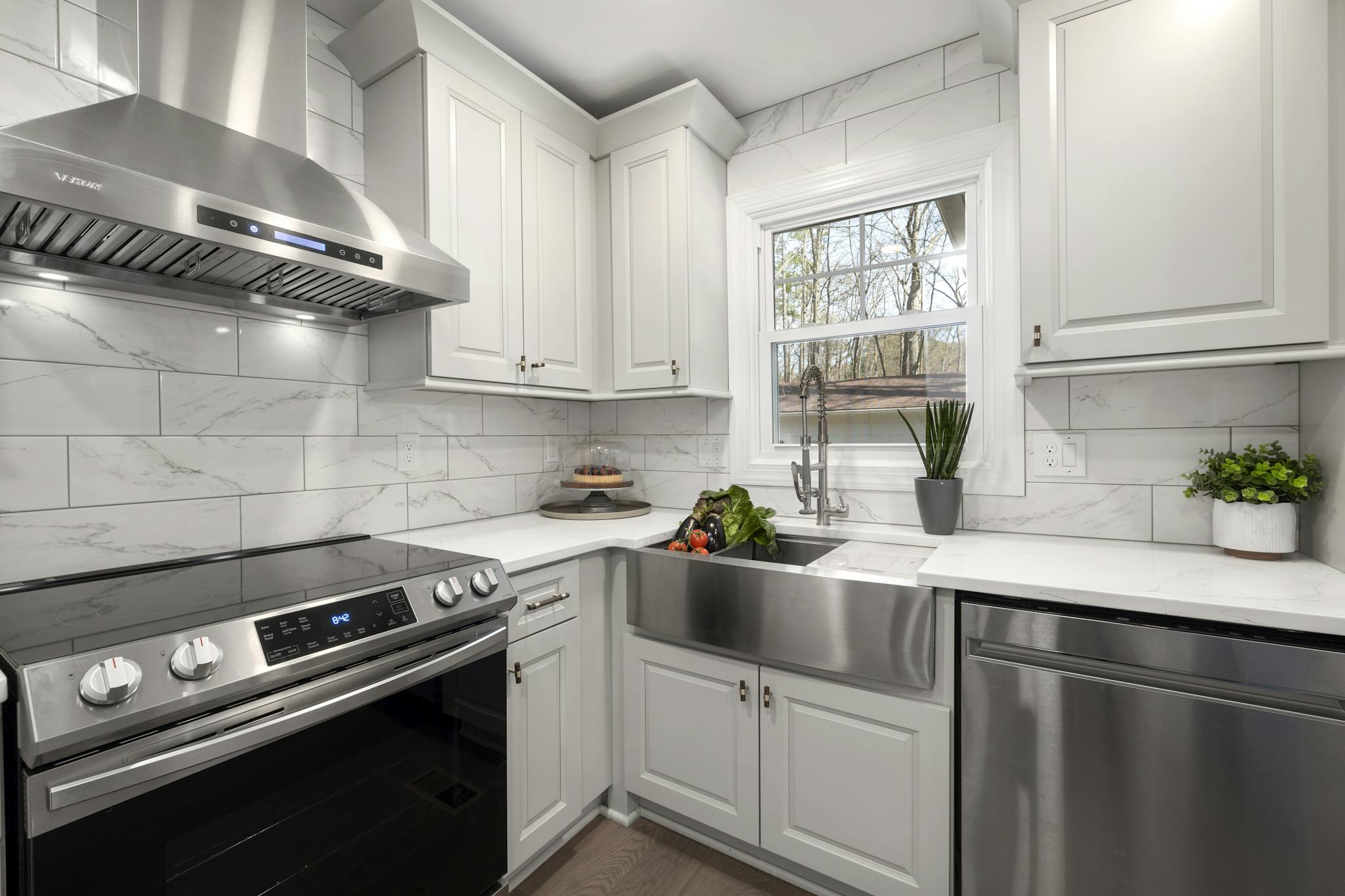 Stylish white kitchen featuring a stainless steel oven, sink, and range hood. Bright and contemporary design.